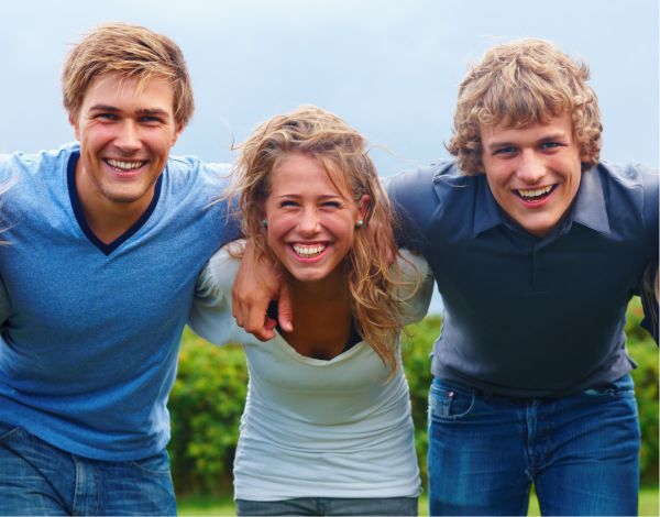 Praktikum Eventmanagement – Rein ins Outdoor-Abenteuer! Drei junge Erwachsene lachen Arm in Arm in die Kamera