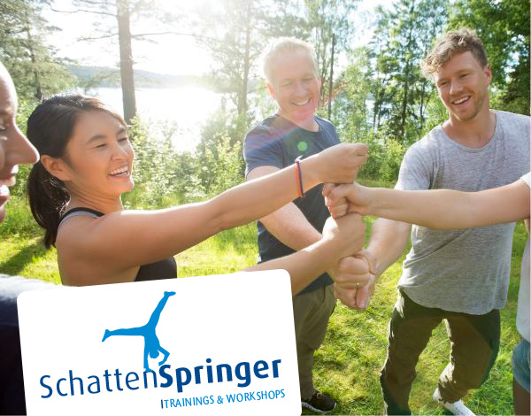 Ein Team steht im Kreis und bildet gemeinsam mit ihren Fusten einen Turm - Dazu wird das Logo von Schattenspringer Trainings und Workshops eingeblendet